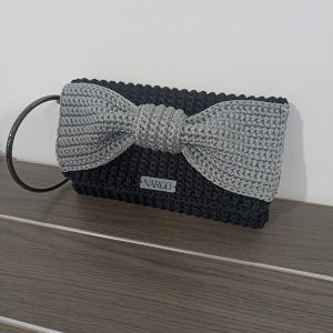 Χειροποίητη πλεκτή μαύρη τσάντα φάκελος με γκρι φιόγκο και μαύρα μεταλλικά στοιχεία.